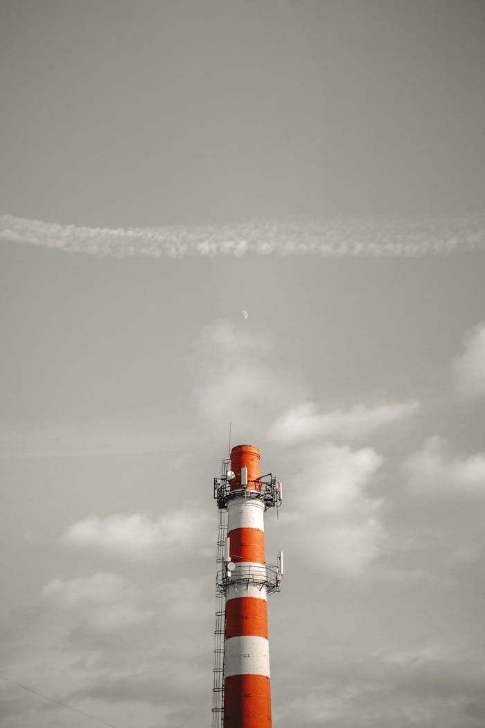 Red and white striped industrial chimney emitting smog under a cloudy sky, highlighting pollution.